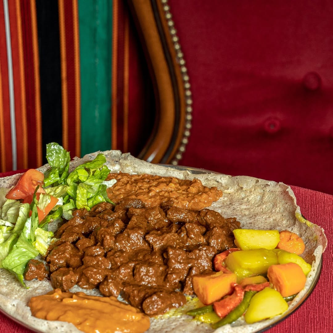 Un vassoio di injera con spezzatino di manzo, purea di lenticchie, verdure e insalata, servito in sala.